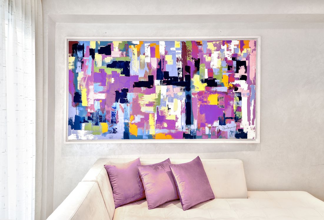 Vibrant abstract painting with bright colors above a white sofa and purple cushi