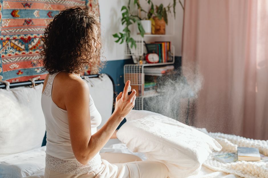 Mulher sentada na cama borrifando névoa perfumada no quarto