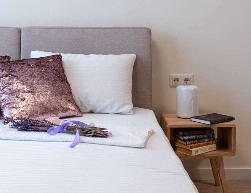 Mesa de cabeceira de madeira com objetos de decoração ao lado da cama