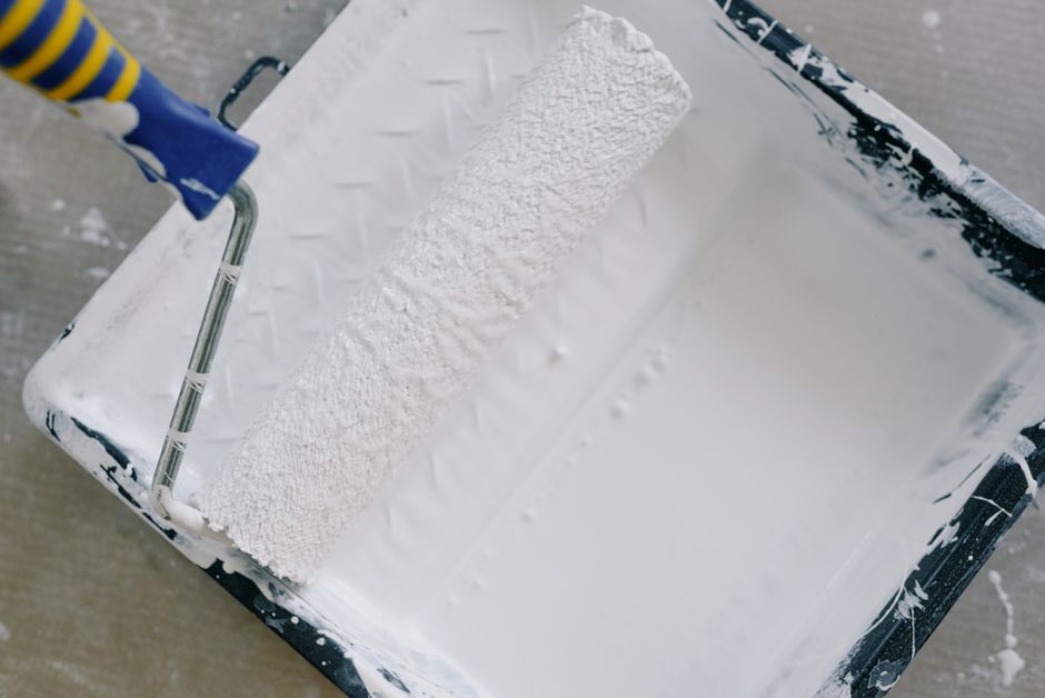 Rolo de pintura apoiado em bandeja preta com tinta branca