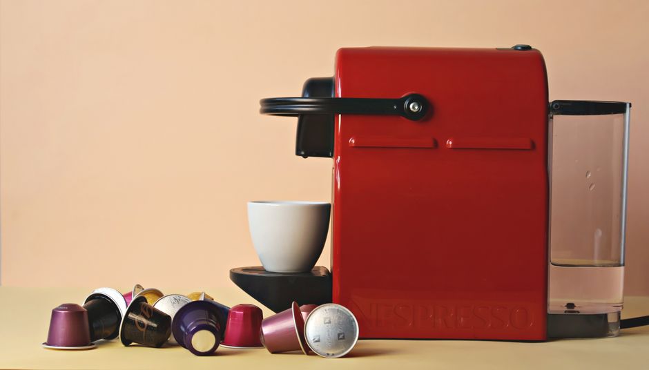 Cafeteira de cápsula vermelha com cápsulas de café organizadas ao lado