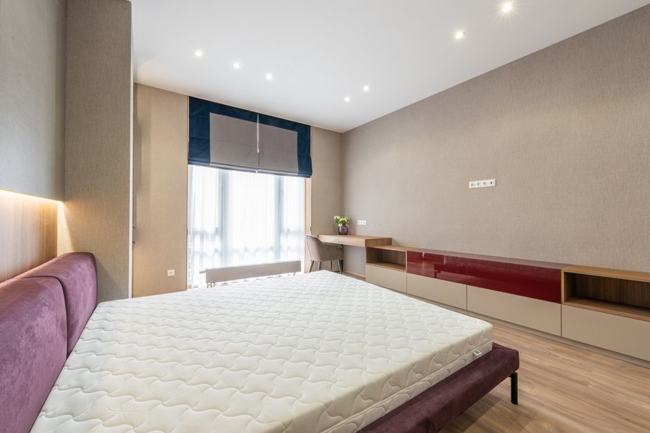 Colchão branco sem roupa de cama sobre a base, em quarto com móvel de madeira