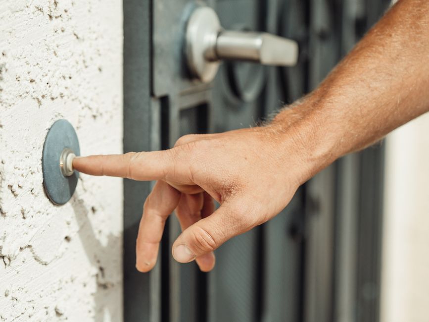Dedo pressionando o botão iluminado de uma campainha inteligente instalada na porta