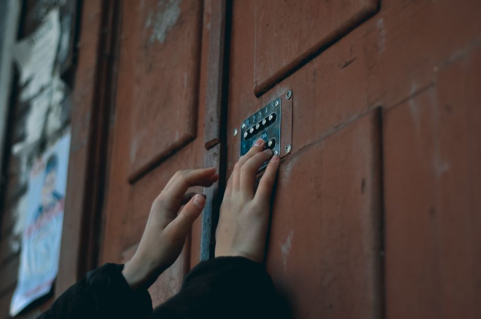 Mão digitando senha em teclado de fechadura digital instalada em porta de madeira