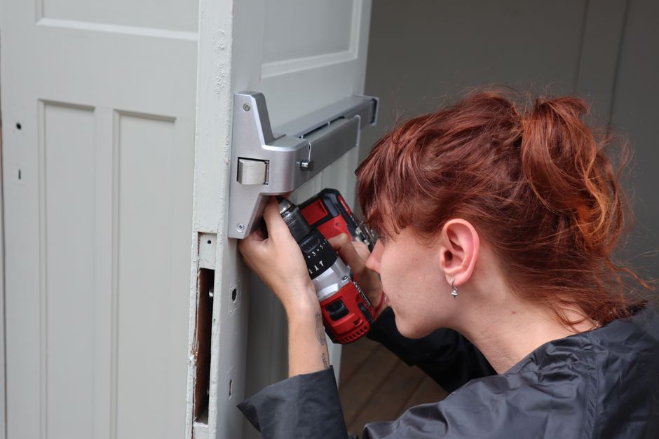 Pessoa instalando fechadura na porta com parafusadeira elétrica