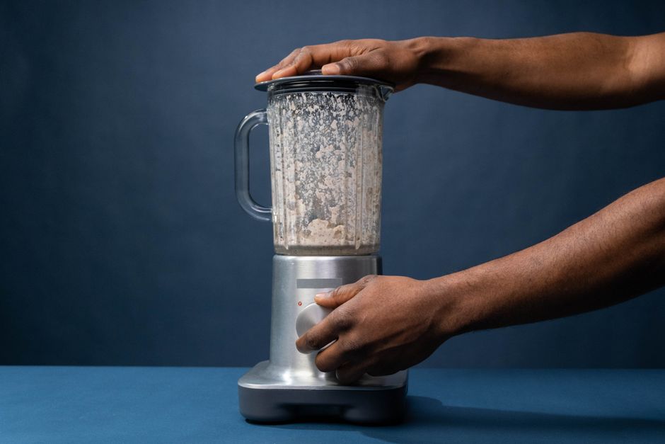 Mãos operando um liquidificador simples de jarra plástica em uma cozinha
