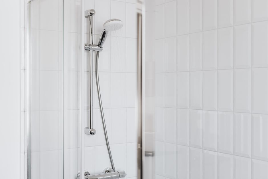 Chuveiro cromado em banheiro com azulejo branco