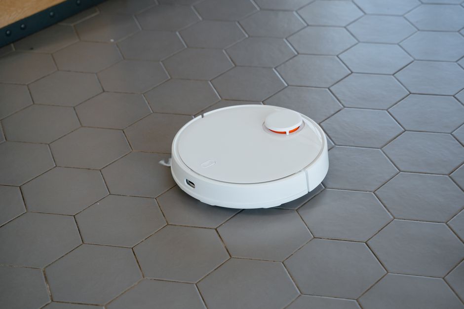 Aspirador robô branco sobre piso de ladrilho hexagonal