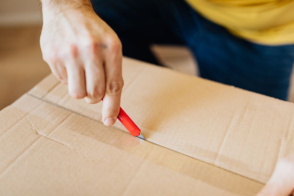 Mão usando estilete para cortar caixa de papelão
