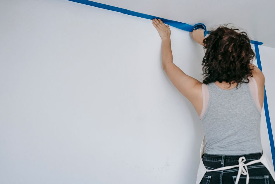 Pessoa aplicando fita crepe na parede para delimitar a área de pintura