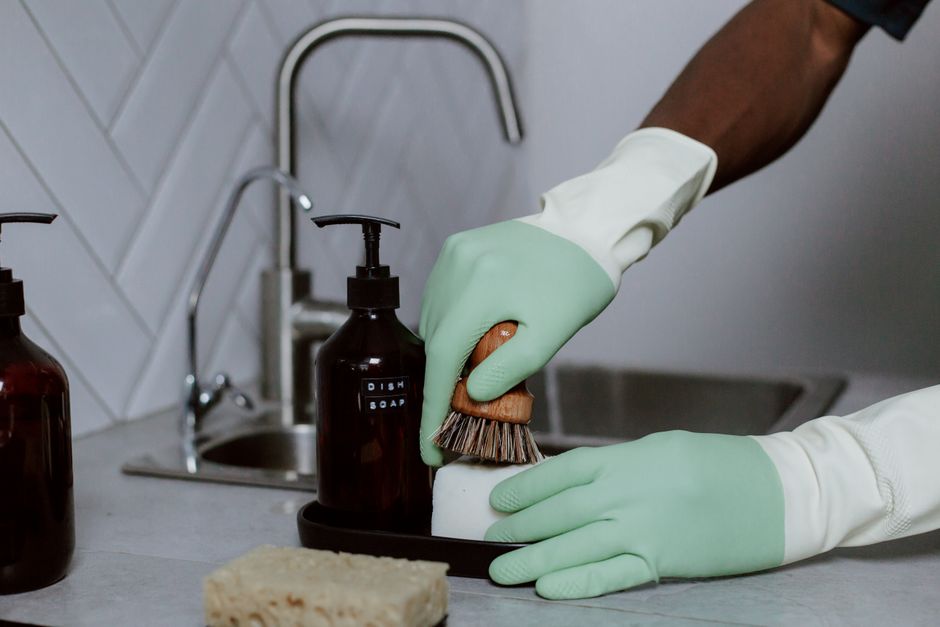Mãos com luvas lavando louça com espuma na pia da cozinha