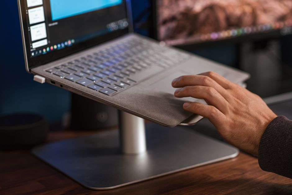 Pessoa digitando em notebook elevado por suporte, na altura dos olhos